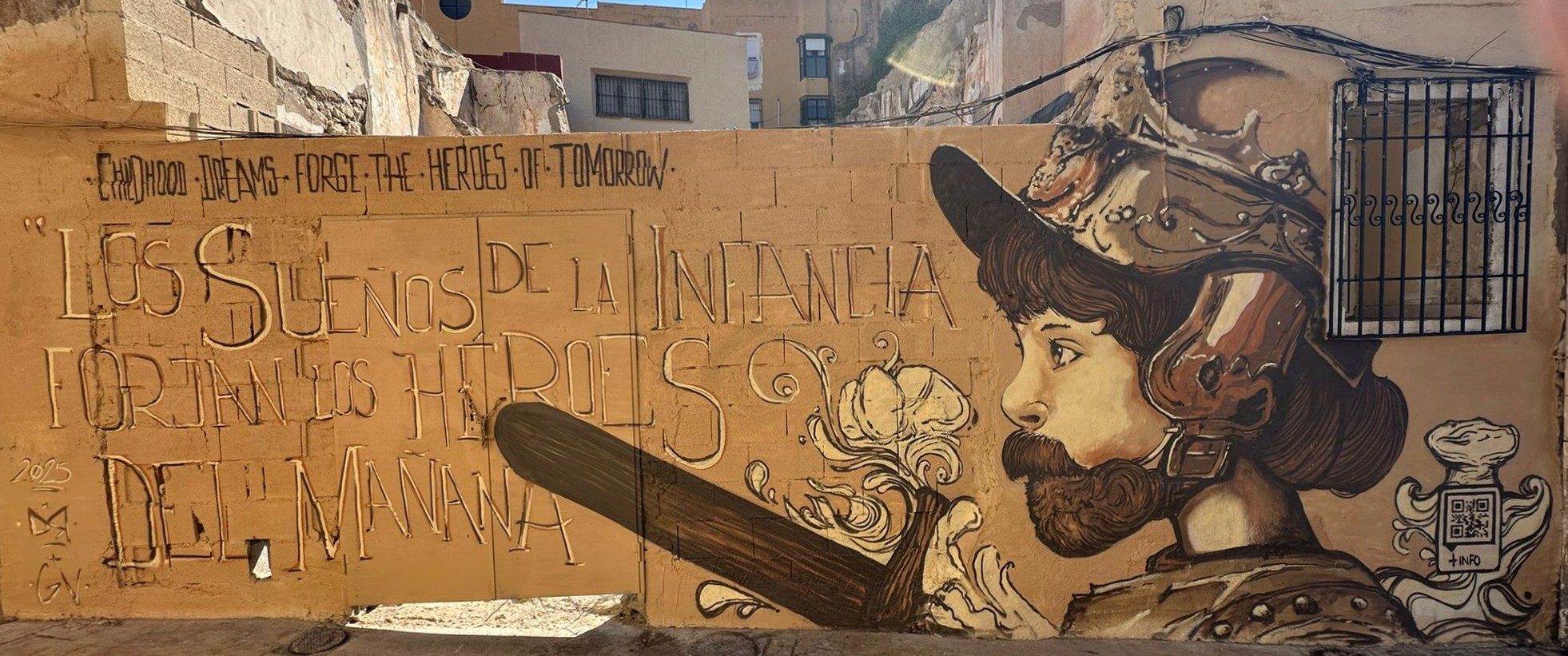 Mural en tonos sepia de un niño con casco histórico mirando a la derecha, flores y la frase ‘Los sueños de la infancia forjan los héroes del mañana.’ sobre una pared urbana en Melilla.